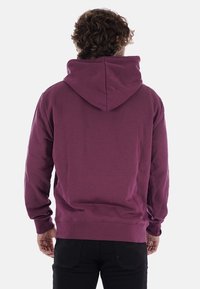Sudadera morada con una gran capucha, puños acanalados y dobladillo. Fabricada con material suave, presenta un corte relajado y un diseño liso, sin patrones visibles.