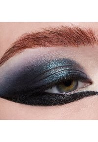 Close-up of an eye with dark blue and black eyeshadow, shimmering highlights, and a bold black eyeliner. Hair is reddish-brown, neatly groomed.