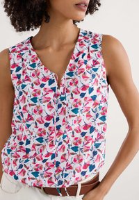 Top senza maniche con scollo a V, caratterizzato da un motivo floreale multicolore con accenti rosa, blu e verde su sfondo bianco.