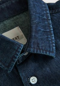 Donkerblauwe denim shirt met een button-down kraag, witte knopen en subtiele textuurvariaties in de stof.