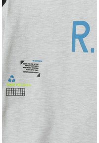 Pilkas sportinis marškinėlis su juodais akcentais, kuriame pavaizduota mėlyna raidė "R." ir įvairūs juodos bei žalios spalvos spausdinti tekstai.