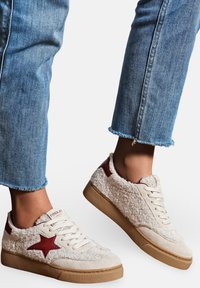 Baskets crèmes avec une texture duveteuse, accent d'étoile rouge et semelle en caoutchouc beige ; lacets et col rembourré pour un confort supplémentaire. Jean en denim avec ourlet effiloché.