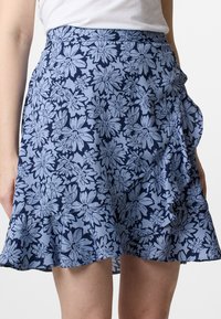 Gonna avvolgente blu floreale con orlo arricciato, realizzata in tessuto leggero con un motivo di grandi fiori blu scuro su uno sfondo azzurro.