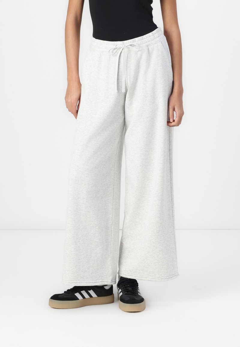 Lys grå sweatpants med en vid ben-design, elastisk talje og snoretræk. Sammen med sorte sneakers med hvide striber.