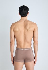 Bruine katoenen boxershorts met een zachte textuur en een Calvin Klein-logo op de tailleband, gedragen door een mannelijke model van achteren bekeken.