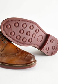 Pantofii de dress din piele maro, cu un design brogue, prezintă detalii perforate și o talpă din cauciuc bordeaux cu indentări circulare.