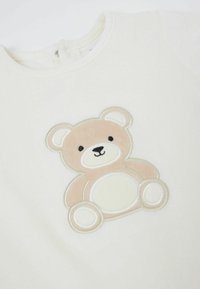 Sweat-shirt couleur crème avec un ours en peluche brodé en beige doux et blanc, avec des accents noirs pour les traits du visage.