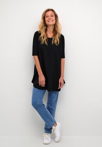 Tunique noire à manches courtes avec une coupe décontractée, associée à un jean droit bleu clair et des baskets blanches. Tissu lisse et design simple.