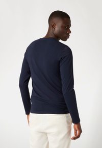 Donkerblauw langemouwen T-shirt van een katoenmix, met een ronde hals en een aansluitende pasvorm, gecombineerd met crèmekleurige broek.