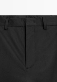 Schwarze maßgeschneiderte Hose mit flachem Bund, Gürtelschlaufen und Reißverschluss. Der Stoff wirkt glatt mit einem leichten Glanz.