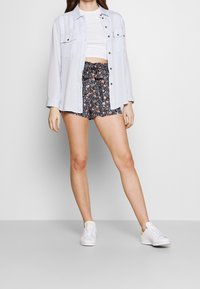 Světle modrá košile s knoflíky přes bílý crop top, doplněná tmavými květinovými šortkami a bílými teniskami. Obsahuje elastický pas se stahovací šňůrkou.