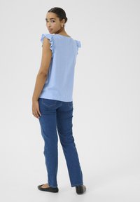 Haut sans manches bleu clair avec des accents de volants aux épaules, assorti à un jean droit bleu foncé et des ballerines noires. Design épuré et minimaliste.