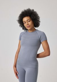 Top atletico grigio a maniche corte con un design aderente, texture liscia e dettagli sottili sulle spalle e sul torso, abbinato a leggings coordinati.