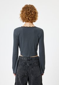 Langärmeliges, dunkelgraues Cropped-Top mit Rundhalsausschnitt und einer schwarzen Spitzenborte am Kragen. Kombiniert mit dunklen Cargo-Hosen.