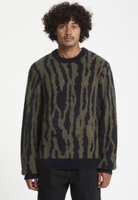 Pull en maille olive avec des rayures bleu marine, doté d'un col rond, de manches longues et d'un tissu texturé et doux.