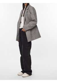 Grå rutiga kavaj med oversized passform, tvåknappsslutning och stora slag, som matchas med svarta cargobyxor och vita sneakers.