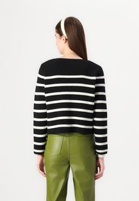 Maglione a righe bianco e nero in maglia con design corto e scollo ampio, abbinato a pantaloni in pelle verde. Tessuto morbido e maniche lunghe.
