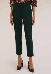 Groene op maat gemaakte broek met een slanke pasvorm, met een gladde textuur, een platte voorkant en een cropped lengte, gecombineerd met donkerrode hoge hakken.