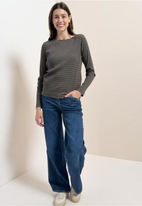 Haut à manches longues rayé noir et blanc, associé à un jean en denim bleu ample et des baskets beige, sur un fond neutre.