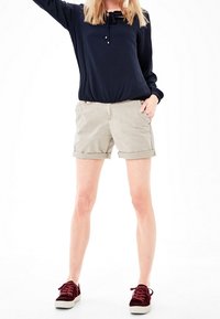 Maglietta a maniche lunghe navy con coulisse, abbinata a pantaloni corti arrotolati beige chiaro e sneakers bordeaux. Design semplice, stile casual.