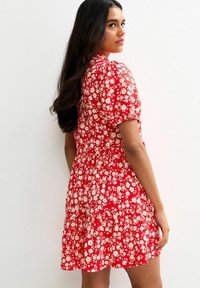 Röd blommig klänning med korta ärmar, med en figursydd bodice och en gathered kjol. Små vita blommor kontrasterar mot den livfulla röda bakgrunden.