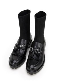 Botas de tobillo de cuero negro con parte superior de tela negra acanalada, que cuentan con borlas decorativas y acabados en plata. Diseño de suela gruesa.