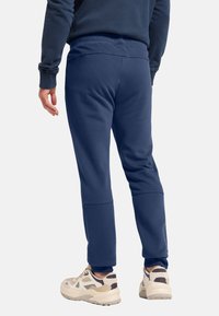 Dunkelblaue Sweatpants mit einer entspannten Passform, weichem Material, gerippten Bündchen und einem dezenten Logo am unteren Bein. Kombiniert mit hellen Sneakers.