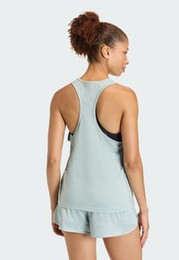 Camiseta deportiva sin mangas de color azul claro con diseño de espalda nadadora, combinada con pantalones cortos a juego que presentan un dobladillo en capas. Textura de tela suave.