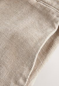 Gros plan d'un tissu chevron beige avec texture de tissage visible et couture cousue sur un matériau doux et plié.