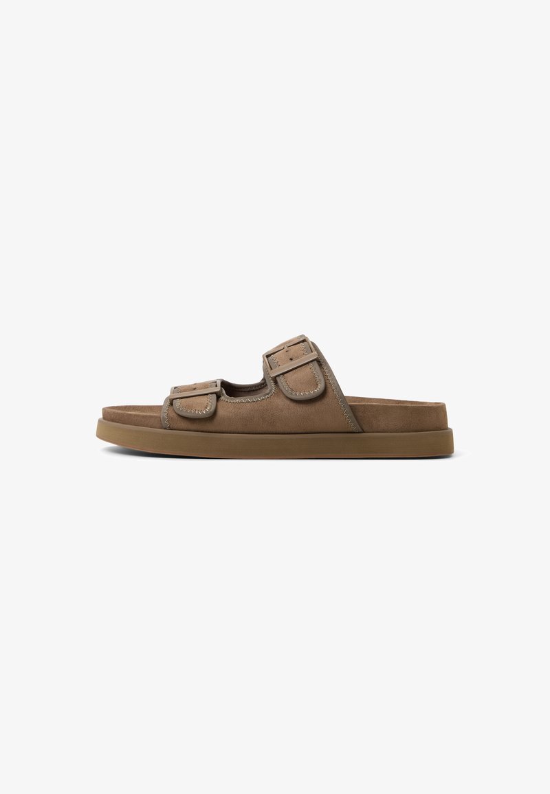 Brown suede slip-on sandal with two adjustable straps, contrasting stitching, and a cushioned rubber sole. Flat footbed design.