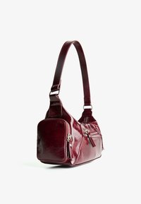 Small glossy dark red handbag with one shoulder strap and two zippered pockets, shown at a side angle on white background.