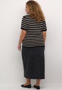 Pruhovaný pletený top v černé a krémové barvě, s krátkým rukávem, spárovaný s tmavými džíny maxi sukně. Celkový look doplňují ploché černé boty.