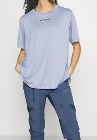 Ljuslila kortärmad skjorta med rundad halsringning, försedd med "TERREX"-logotypen i svart. Bärs tillsammans med mörkblå, mjukt texturerade byxor.