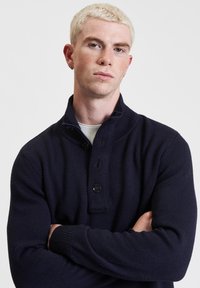 Maglione lavorato a maglia di colore blu navy con colletto alto, dotato di patta con bottoni, tessuto testurizzato e polsini a costine. Design aderente.