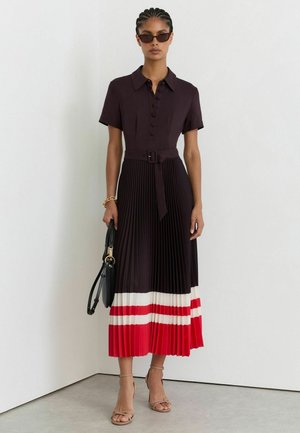Donna che indossa un vestito midi plissé con top nero, gonna a righe rosse e bianche, occhiali da sole, tacchi color nude e tiene una borsa nera.