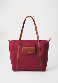 Maroon nylon tote bag with brown leather straps and pocket. Features a gold snap closure on the front pocket. Smooth texture, minimalist design.