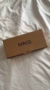 Caja de cartón marrón con cierre de solapa, que presenta las letras "MNG" impresas en negrita y en un color oscuro en la superficie superior.