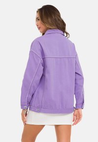 Lila Jeansjacke mit lässigem Schnitt, großem Kragen und Knopfmanschetten. Mit Kontrastnähten und zwei Seitentaschen ausgestattet.
