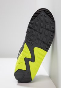 Podešev tenisky Nike s černým gumovým vzorem, jasně žlutými akcenty a texturovanými protiskluzovými prvky. Výrazné logo Nike na boku.