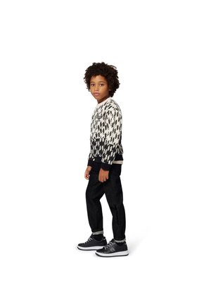 Sweatshirt com padrão preto e branco, com punhos canelados, combinado com calças de ganga escuras e ténis pretos com solas brancas.