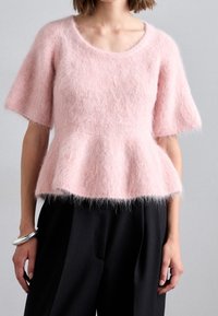 Růžový chlupatý peplum svetr s krátkými rukávy, vyrobený z měkkého, texturovaného materiálu. Má kulatý výstřih a mírné rozšíření v pase.