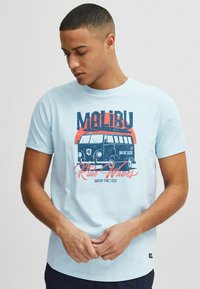Világoskék, rövid ujjú pamut póló, vintage kisbusz grafikával, rajta "MALIBU" és "Ride Waves" felirat sötétkékkel és pirossal.
