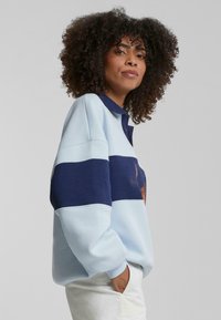 Polo-lignende sweatshirt i lys blå og marineblå striper, med krage som kan knytes opp og teksturert stoff. Casual passform med ribbestrikkede mansjetter.