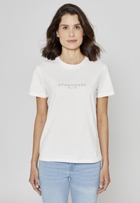 T-shirt en coton blanc avec manches courtes et encolure ronde, portant l'inscription "STRENESSE BLUE" en gris clair sur la poitrine.