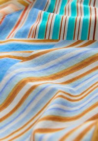 Stof med bølget striber i orange, blå, blågrøn og hvid, der viser en glat tekstur og bløde folder.