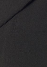 Zwarte stof met een gladde textuur. Bevat naden en een klein, schuin pocketdetail, wat een strakke, minimalistische uitstraling creëert.