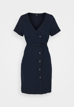 Syvytön, pehmeästä kankaasta valmistettu tummansininen kietaisumekko, jossa on V-pääntie, lyhyet hihat, vyö soljella ja kultaiset napit edessä.