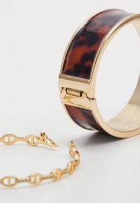 Tortoiseshell bangle with gold hardware alongside a gold chain bracelet featuring oval links and a lobster clasp. Both jewelry pieces are shiny.