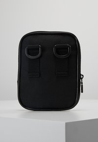 Czarna torba materiałowa o prostokątnym kształcie, wyposażona w dwie pętle na górze, gładką fakturę i zamek błyskawiczny po bokach.