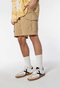 Beige cargo shorts with large side pockets, paired with white and tan sneakers featuring black accents and white crew socks.